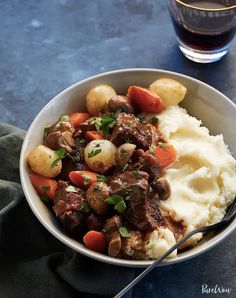 a bowl filled with meat, potatoes and carrots next to a fork on a table