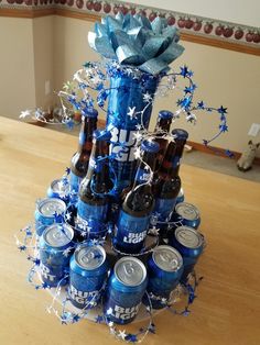 a tower made out of beer cans and wrapped in blue ribbon with flowers on top