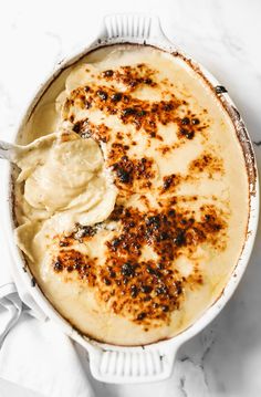 a white dish filled with mashed potatoes on top of a marble countertop next to a spoon