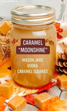 a mason jar filled with caramel squares next to some pine cones and pumpkins