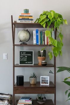 a bookshelf with plants and pictures on it in the corner of a room