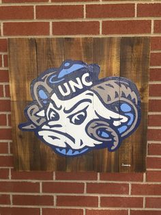 a wooden sign with the word unc painted on it in front of a brick wall