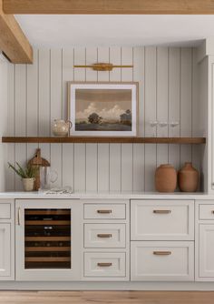 a kitchen with white cabinets and wooden shelves, an open wine bottle rack is on the far wall