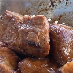 some meat is being cooked in a frying pan with brown sauce on the side