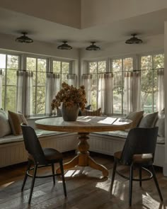 a dining room table with four chairs and a bench in front of the bay window