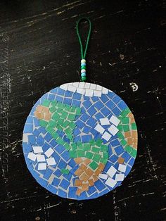 a blue and green mosaic ornament hanging from a string on a wooden table