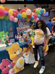 a woman standing next to a child in front of a table with balloons and teddy bears