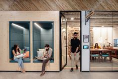 two people are sitting on the couch in an office with glass walls and wood paneling