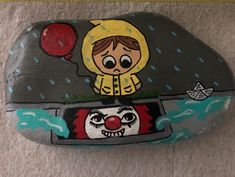 a painted rock with an image of a clown riding a boat in the water and holding a red balloon