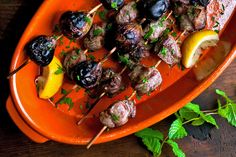 an orange platter filled with meat and veggies on skewers next to lemon wedges