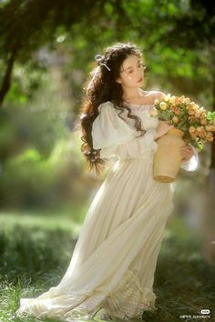 a woman in a white dress holding a basket full of flowers and posing for the camera