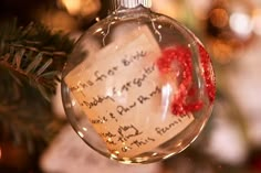 a christmas ornament hanging from a tree with writing on it and a red ribbon