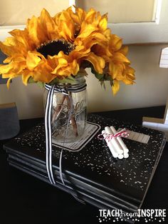 sunflowers are in a mason jar on top of a black table with writing utensils