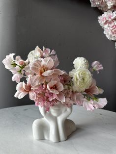 a vase filled with pink and white flowers on top of a marble table in front of a gray wall