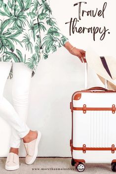 a woman standing next to a white suitcase with the words travel therapy written on it