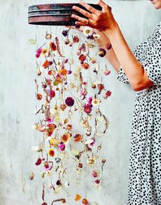 a woman holding a tray with flowers hanging from it's sides, in front of a wall