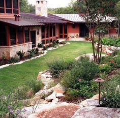 a house that is next to some rocks and grass in the yard with flowers around it