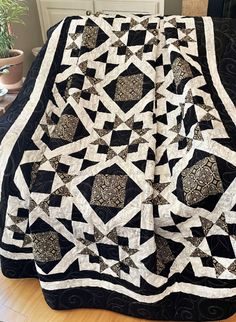 a large black and white quilt on top of a wooden floor next to a potted plant