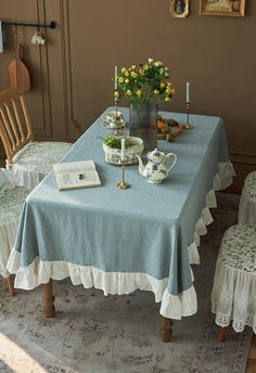 a blue table cloth with white ruffles on it and flowers in a vase