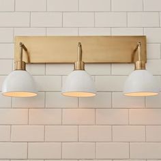 three lights are on the wall in front of a white brick wall with gold trim