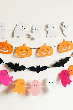 paper bats, ghostes and pumpkins are hanging from a string on the wall