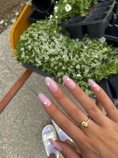 a woman's hand with pink and white nail polish on her nails, next to potted plants