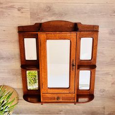 an old wooden medicine cabinet with three mirrors on it's sides and a potted plant next to it