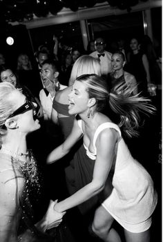 black and white photograph of two women dancing at a party with people in the background