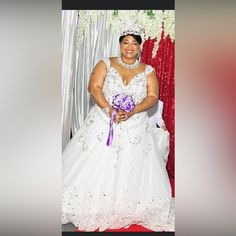 a woman in a white wedding dress holding a purple bouquet and posing for a photo