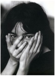 a black and white photo of a woman covering her face with both hands while looking at the camera