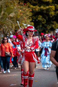 a woman dressed in red and white walking down the street with two sticks on her hip