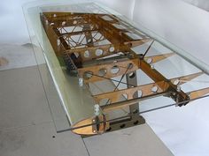 a glass table with a wooden boat on it's side and some metal parts attached to the top