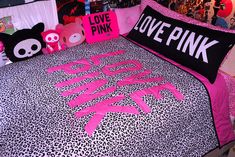 a bed with pink and black pillows on it in a room filled with posters, pictures, and other items