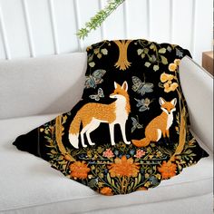 a blanket with two foxes on it sitting on a white couch next to a plant