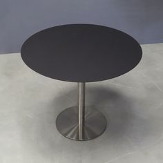 a round table with a metal base sits on a white countertop in front of a gray wall