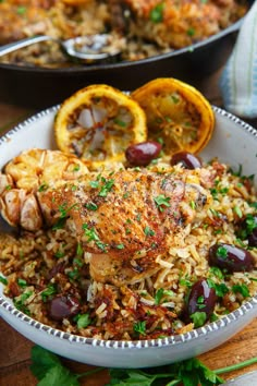 a white bowl filled with rice covered in meat and olives next to an orange slice