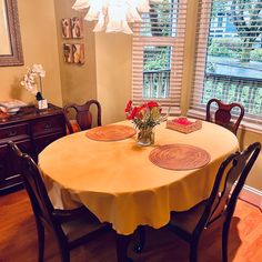 a dining room table with flowers in a vase on the top and chairs around it