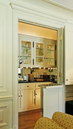 a kitchen with white cabinets and glass shelves in the door way to another room that has a bar