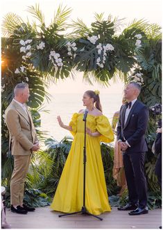 a woman in a yellow dress stands at a microphone as two men stand next to her