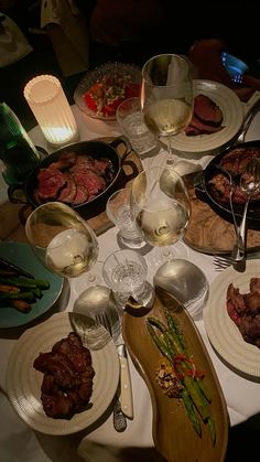 a table topped with plates and bowls filled with food next to glasses of white wine