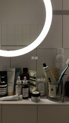 a bathroom counter with various personal care items on it and a round mirror above it