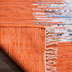 an orange and white rug with fringes on top of wooden flooring next to a wall