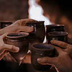 two people are holding cups in front of a fire and another person is reaching for one