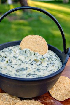 spinach dip in a black bowl with crackers on the side and grass in the background