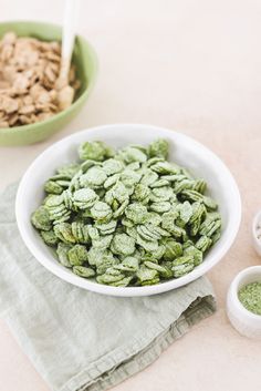 a white bowl filled with green powder next to two bowls of food on a table