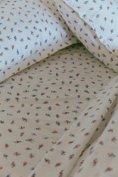 an unmade bed with white sheets and blue and orange flowers on it's edges