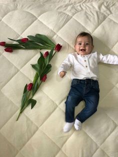 a baby laying on top of a white bed next to red tulips and green leaves