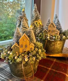 three tin buckets with small houses and trees in them on a plaid table cloth