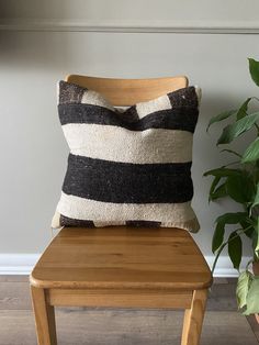 a black and white pillow sitting on top of a wooden chair next to a potted plant