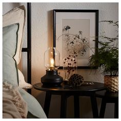 a table with a lamp on top of it next to a plant and a bed